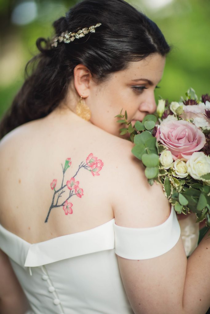 A wedding portrait of a bride with a tattoo on her back holding a bouquet.