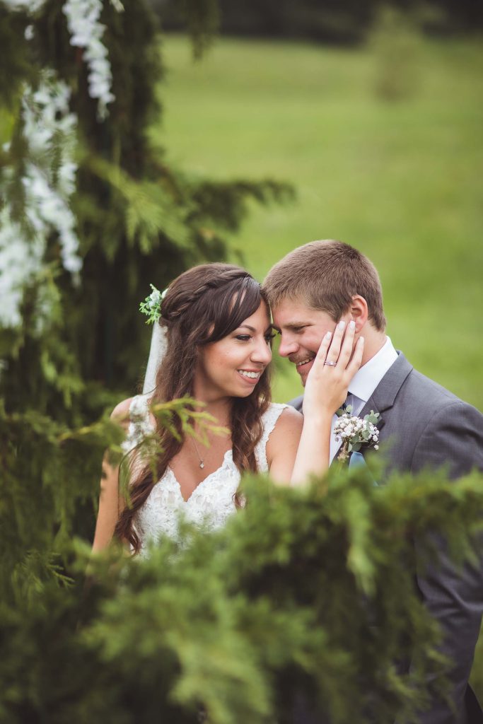 A portrait of a bride and groom embracing in a grassy field at their wedding.