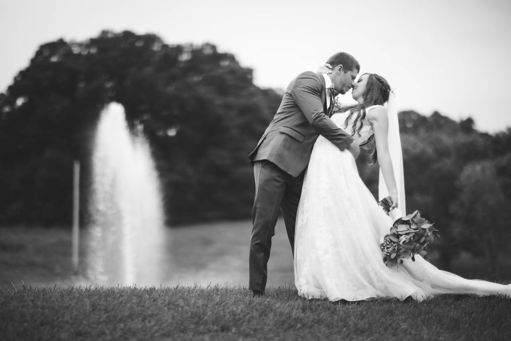 A couple kisses at their wedding ceremony in front of a fountain.