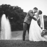 A couple kisses at their wedding ceremony in front of a fountain.