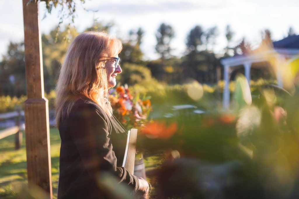 A woman is standing in front of a flower garden during a wedding ceremony.