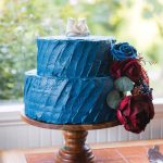 A blue frosted wedding cake on a wooden stand with intricate details.