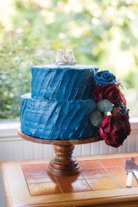 A blue frosted wedding cake on a wooden stand with intricate details.