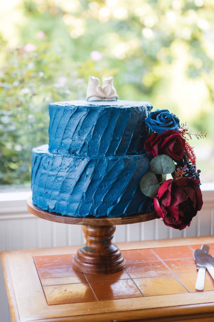 A blue frosted wedding cake on a wooden stand with intricate details.