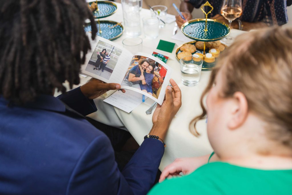 A group of people at a wedding reception sitting at a table looking at a photo.
