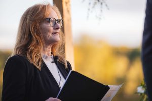 A woman wearing glasses is holding a book at a wedding ceremony.