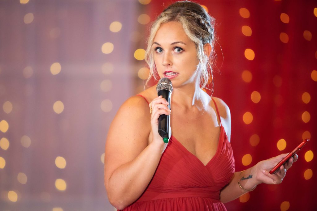 A woman in a red dress speaking into a microphone at a wedding reception.