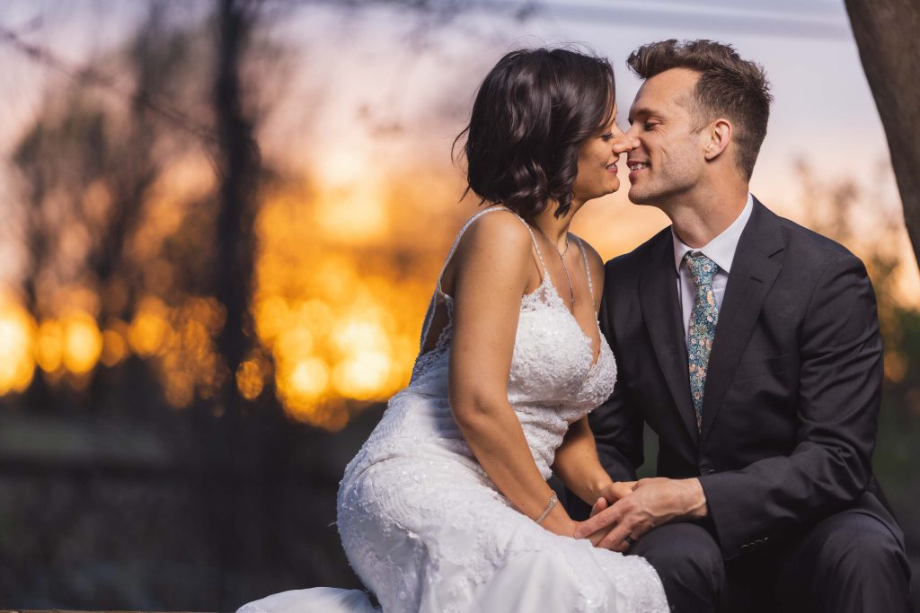 A couple of newlyweds sharing a romantic kiss during their wedding portrait session at sunset.