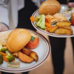 Two people holding plates with wedding food on them.