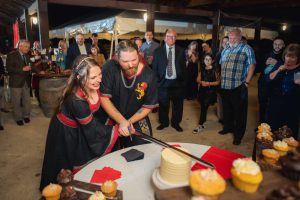 A Wedding couple cutting a cake in front of a crowd at their Reception.