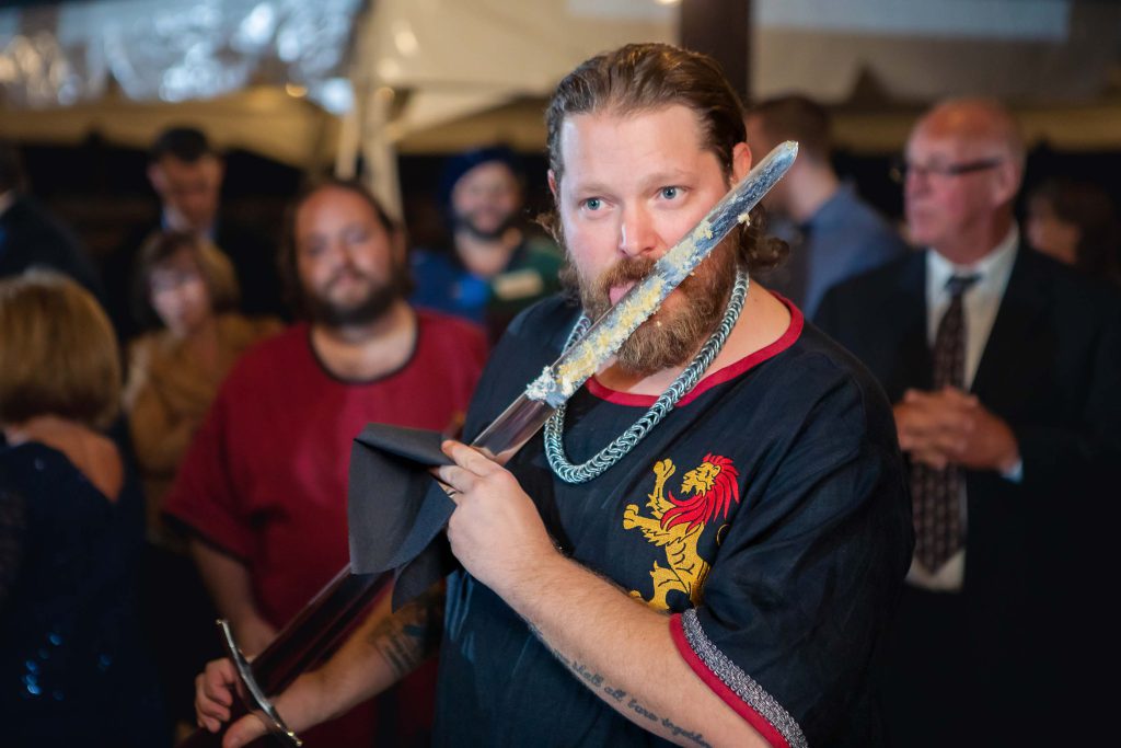 A groom holding a sword during his wedding reception.
