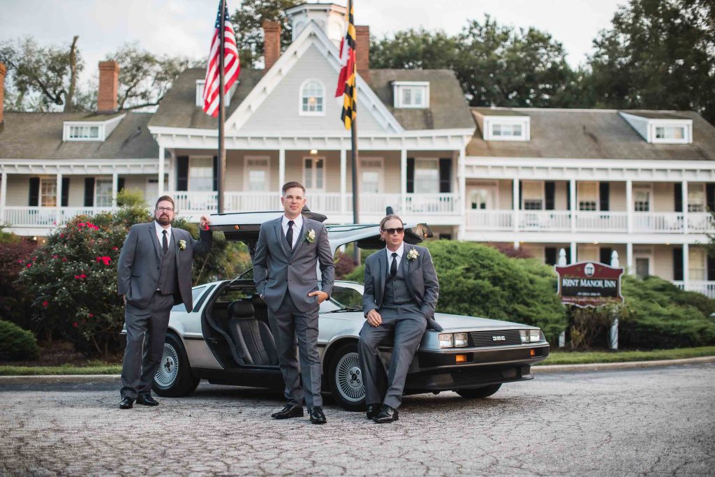 Groomsmen posing next to a Delorean in front of a house at a wedding.