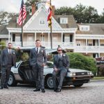 Groomsmen posing next to a Delorean in front of a house at a wedding.