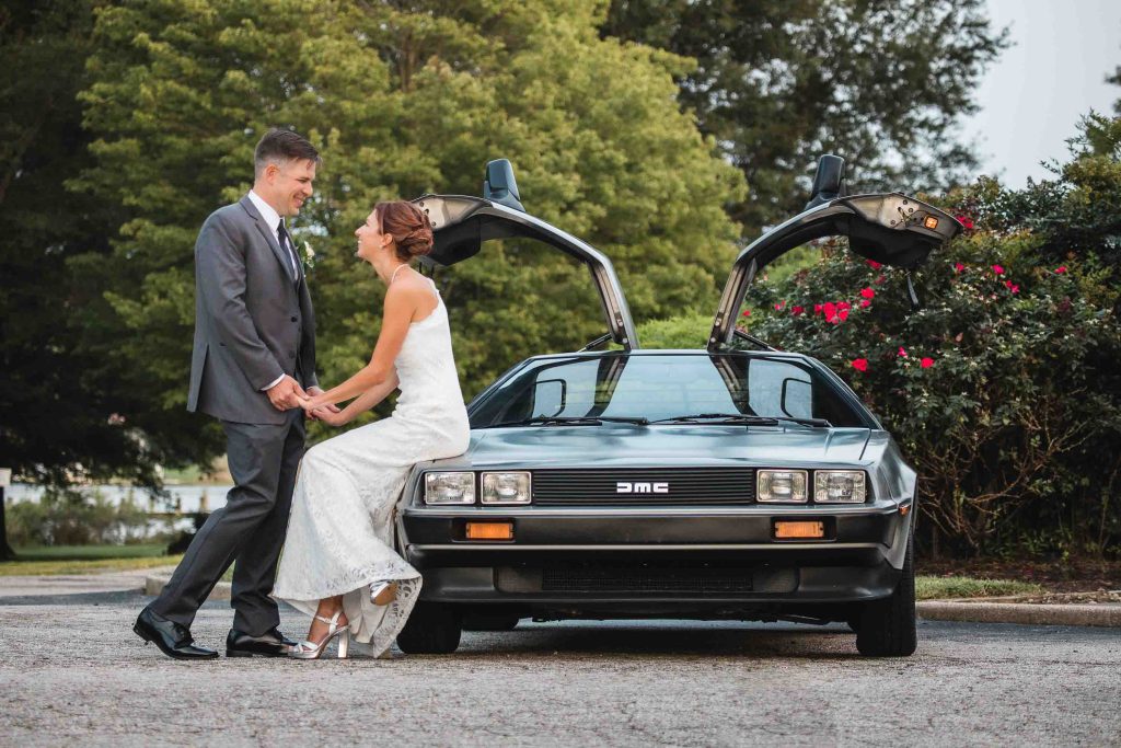 A wedding portrait of a bride and groom standing next to a Delorean car.