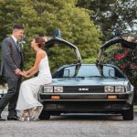 A wedding portrait of a bride and groom standing next to a Delorean car.