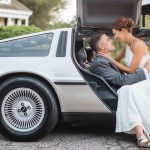 A wedding portrait of a bride and groom kissing in the back of a Delorean.