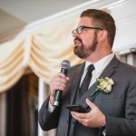 A man in a suit speaking at a wedding reception.