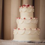 A detailed white wedding cake is sitting on a table.