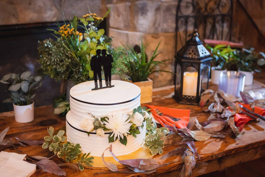 A detailed wedding cake sits on a table next to a fireplace.