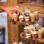 A person is putting wedding cupcakes on a wooden stand, paying attention to details.