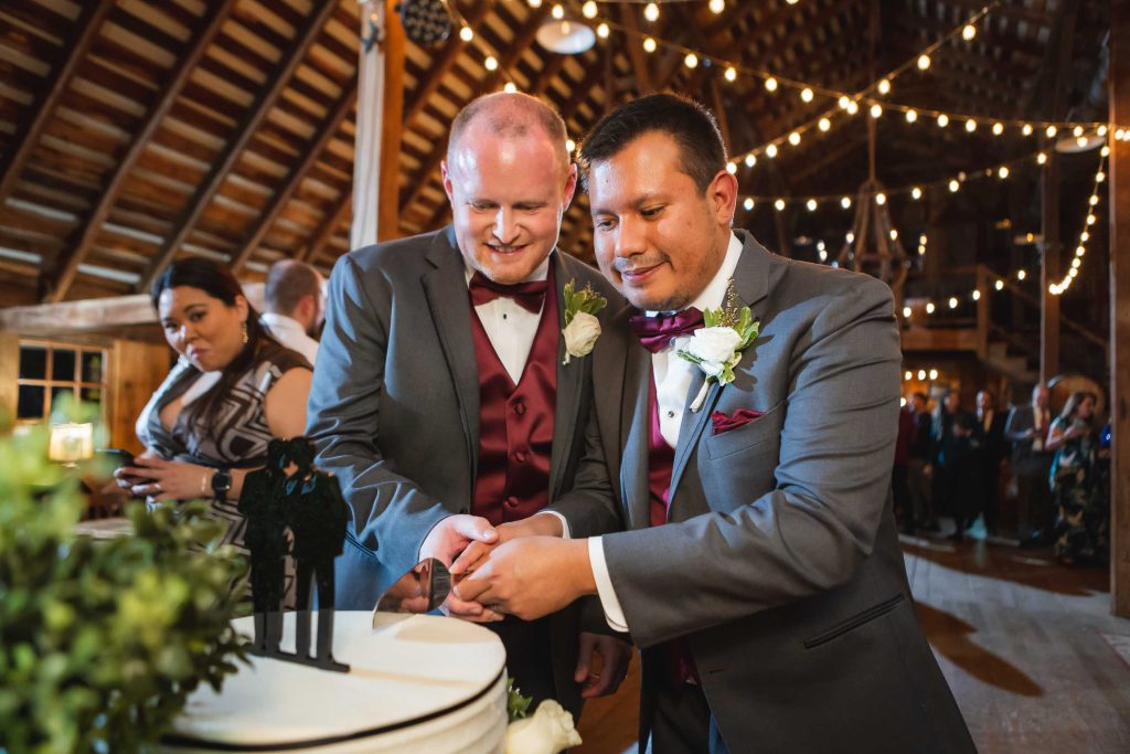 Two men cutting a wedding cake at a reception.