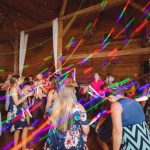 A group of people dancing at a wedding reception in a barn with colorful lights.