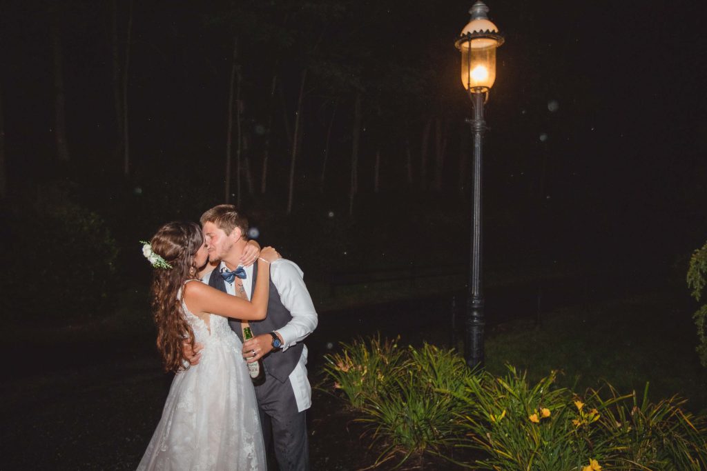 A bride and groom kiss during their wedding reception in front of a street light at night.
