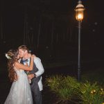 A bride and groom kiss during their wedding reception in front of a street light at night.