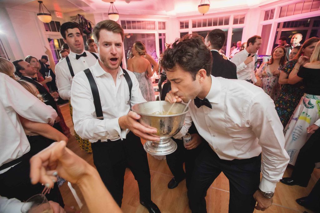 A group of men drinking from a cup at a wedding reception.