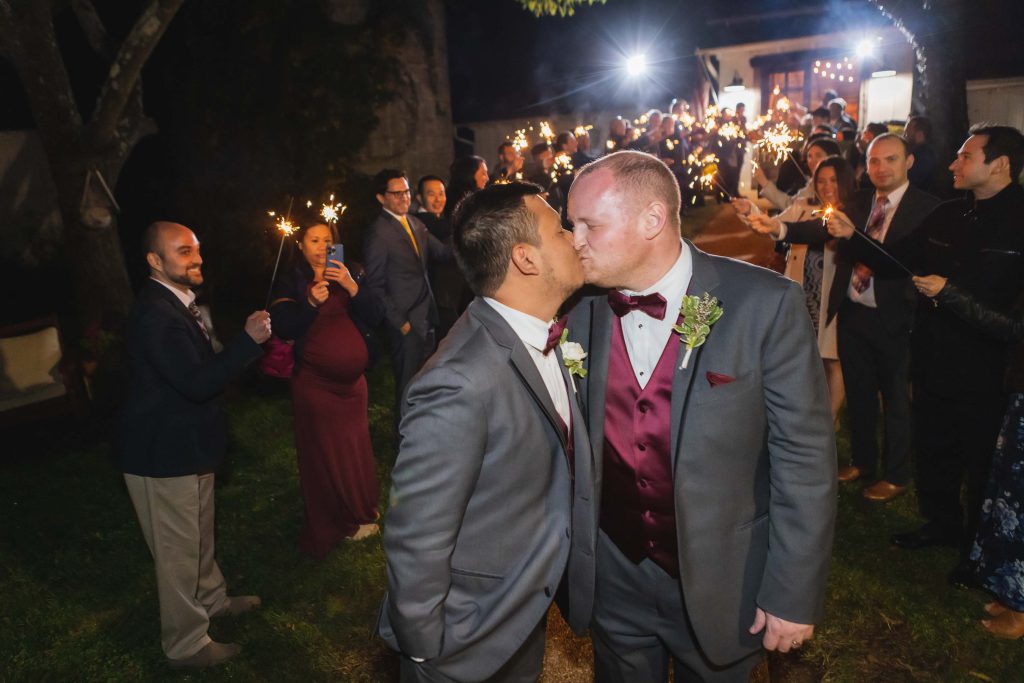 Two grooms kissing at their wedding reception.