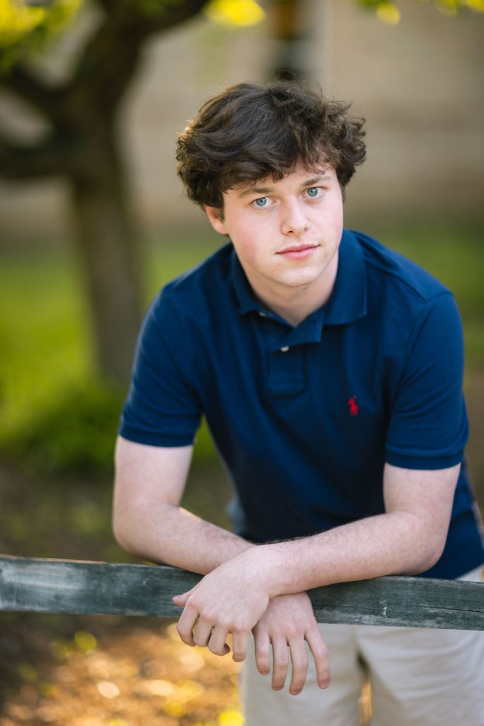 A portrait of a young man leaning against a fence during his graduation.