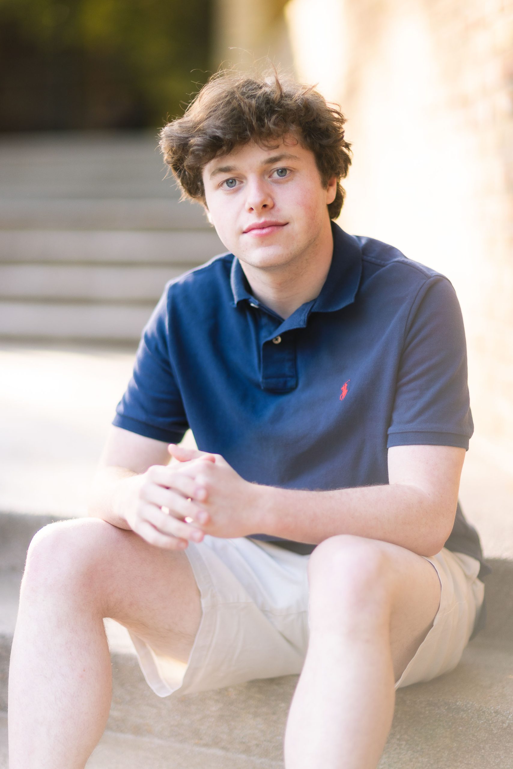 A young man in a blue shirt sitting on steps, captured in a graduation portrait.