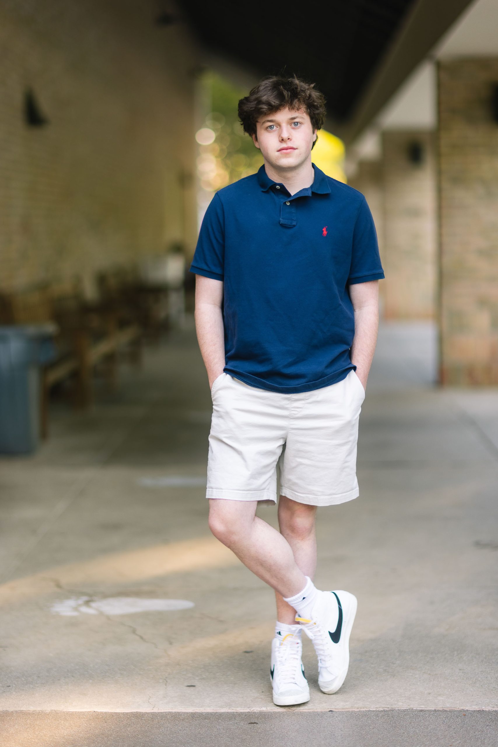 A young man wearing a polo shirt and shorts poses for a portrait.