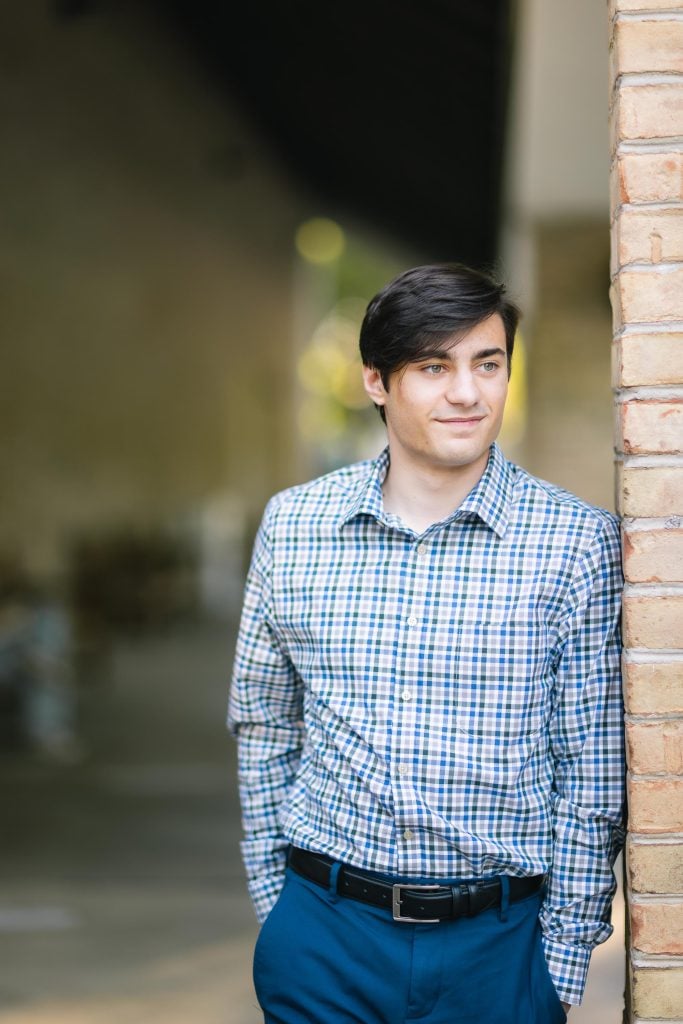 A senior graduate leaning against a brick wall.