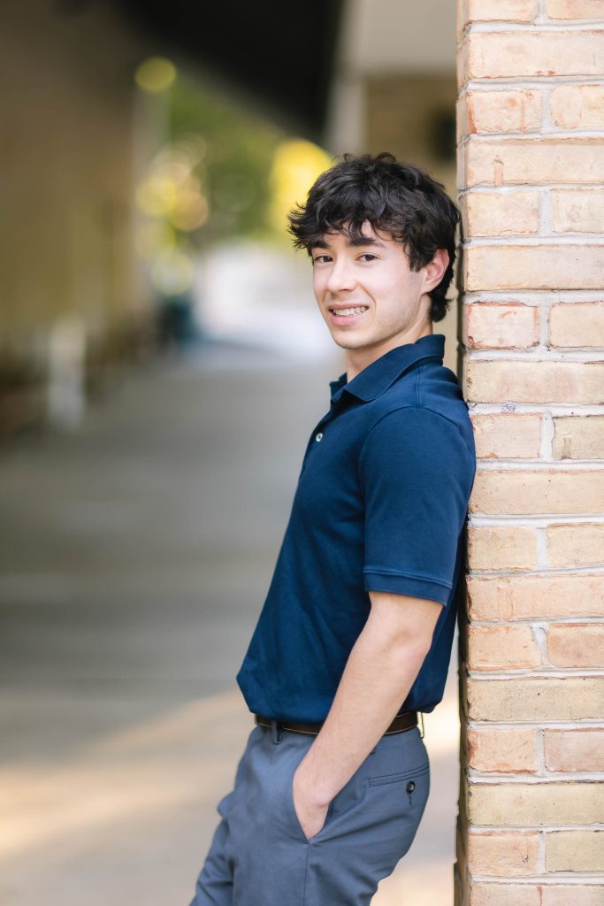 A high school graduate posing for a portrait against a brick wall.