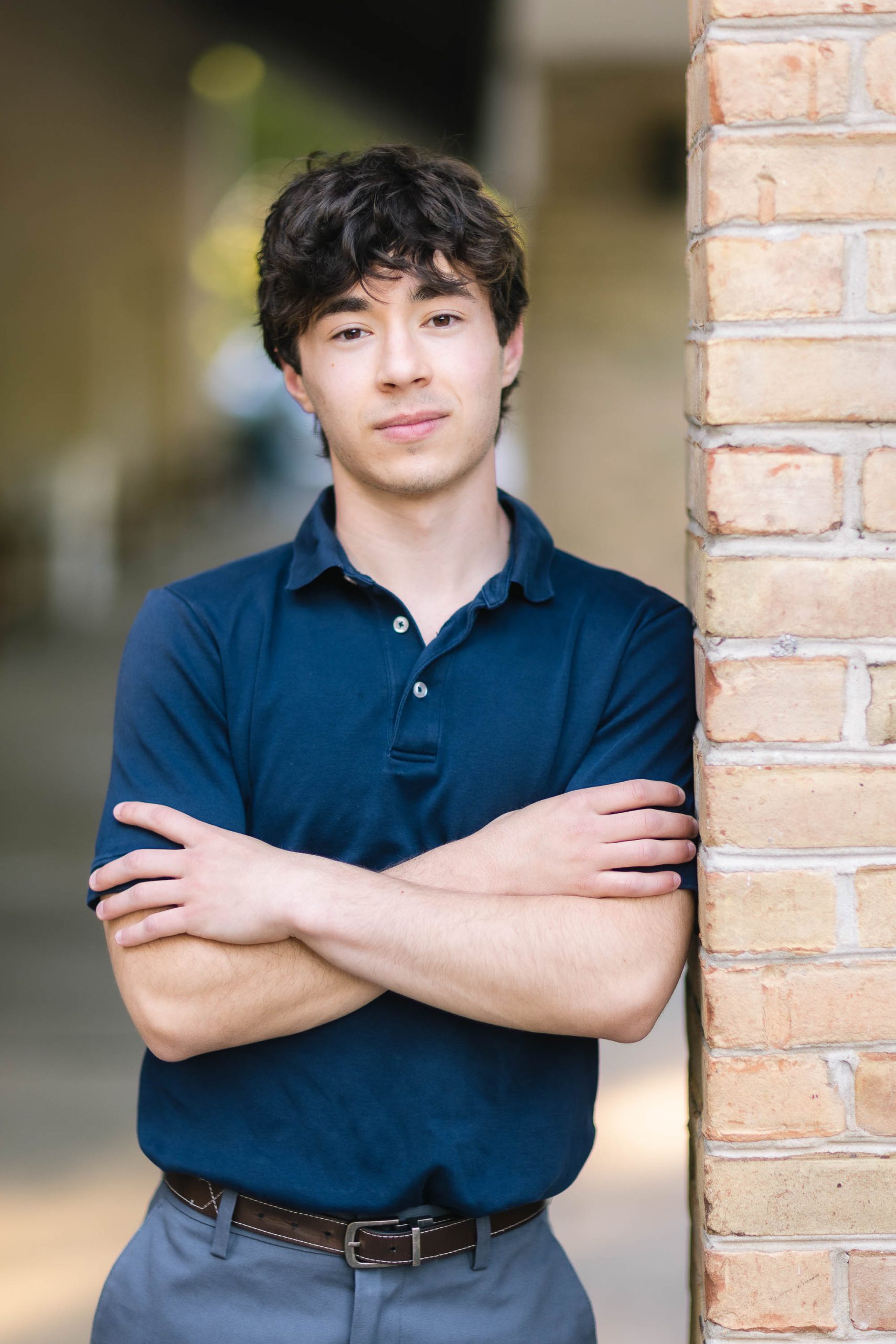 A senior high school student in a blue shirt leaning against a brick wall.