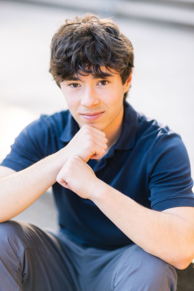 A young man in a blue shirt sitting on steps during his high school graduation.
