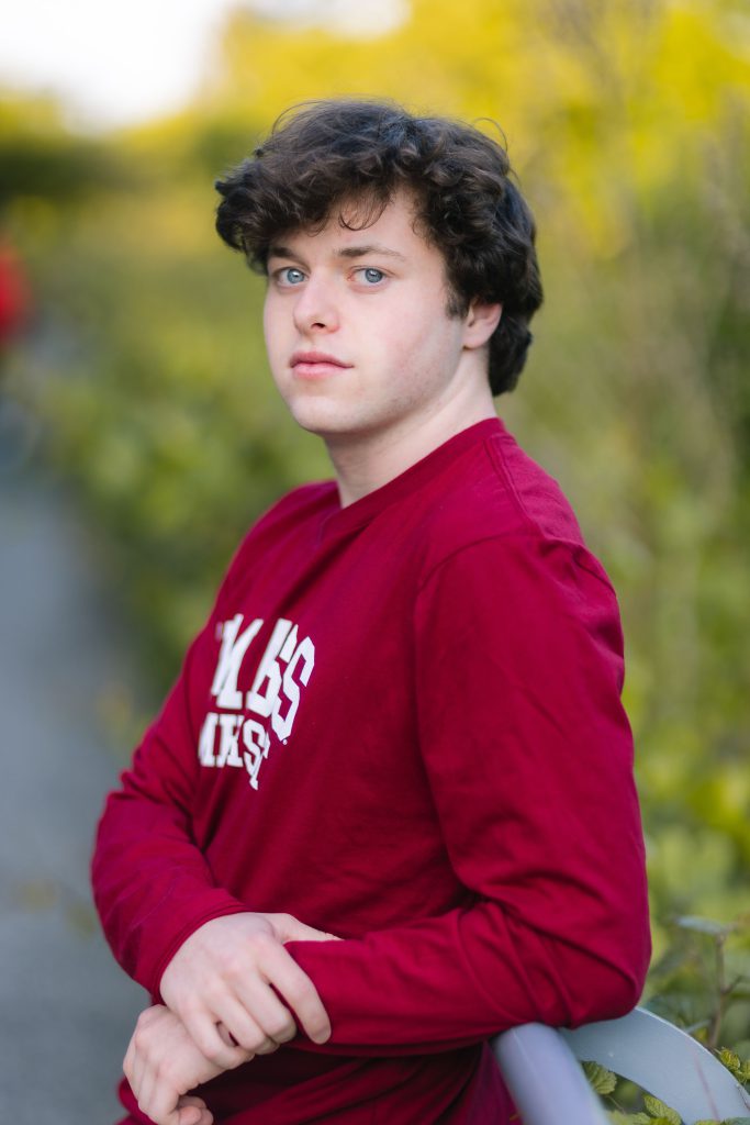 A high school senior in a red shirt leaning against a railing.