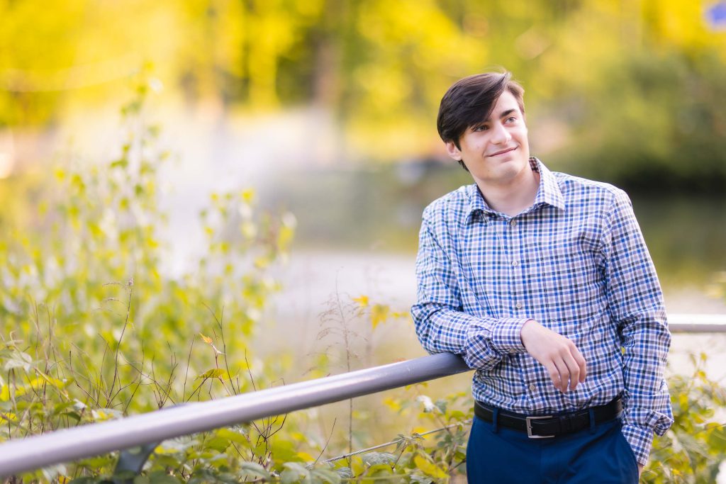 A senior high school student casually posing near a pond.
