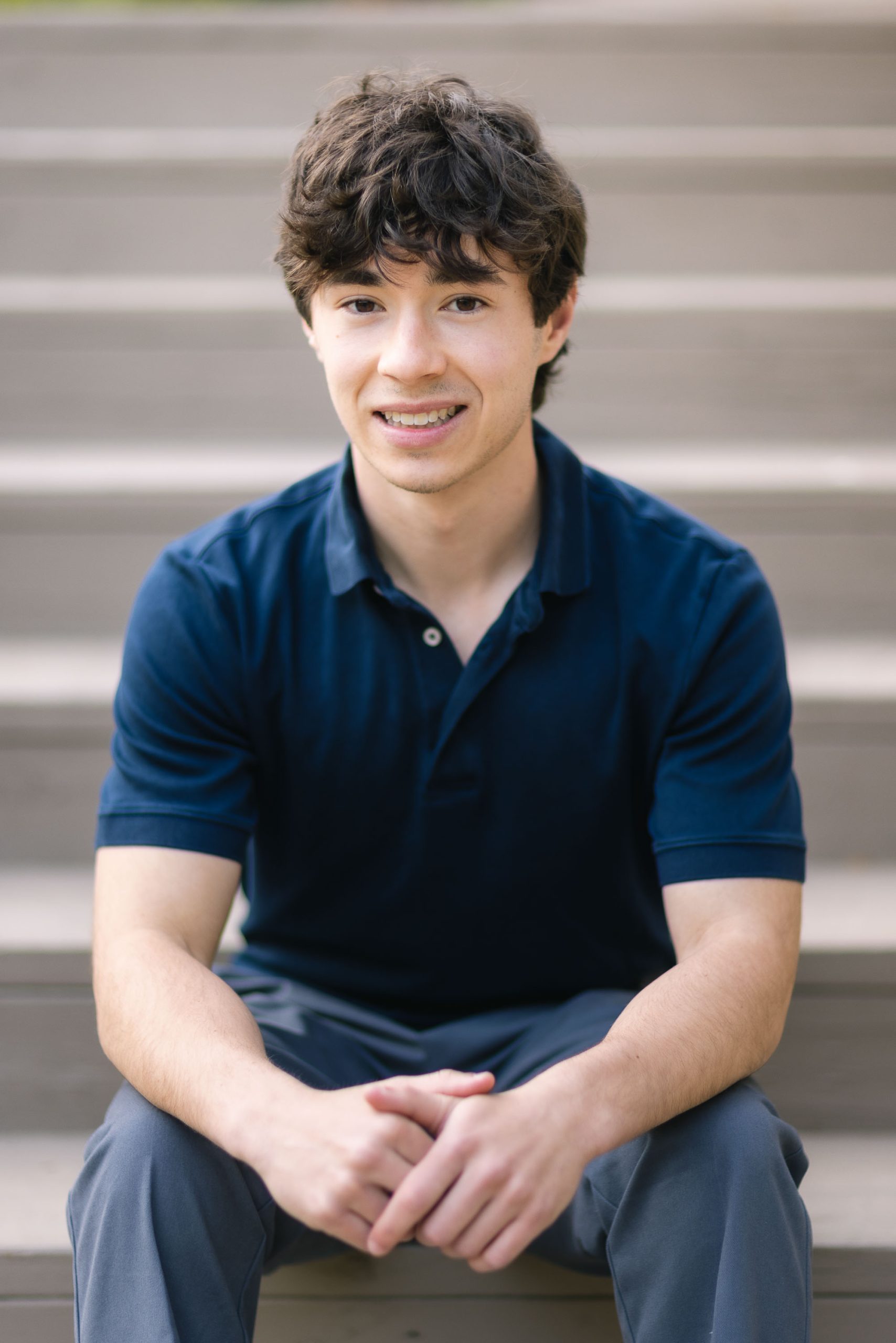 A young man in a blue shirt sitting on steps, potentially in a graduation portrait.