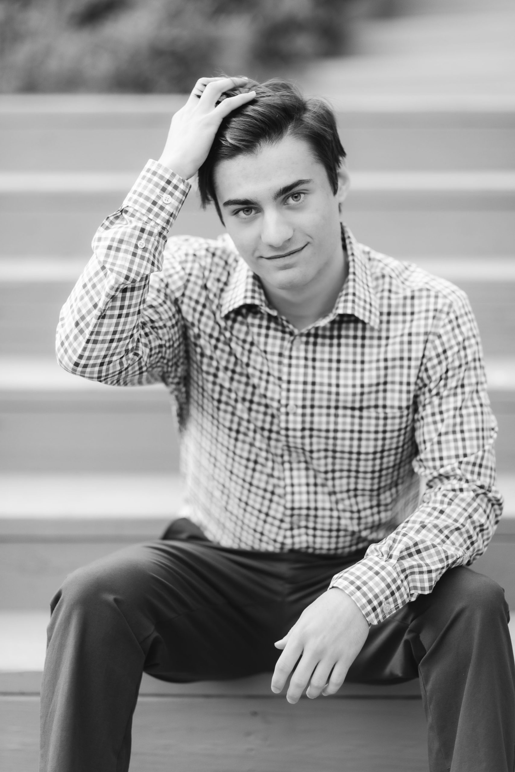 A black and white graduation portrait of a young man sitting on steps.
