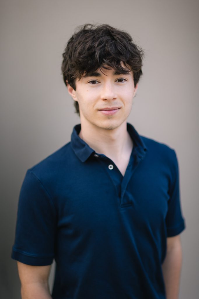 A high school graduate in a blue shirt posing for a graduation portrait.