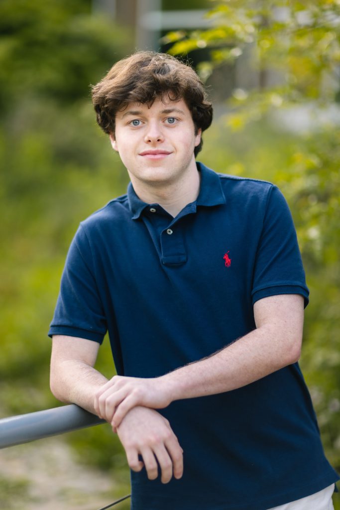 A graduating senior in a blue shirt leaning against a railing.
