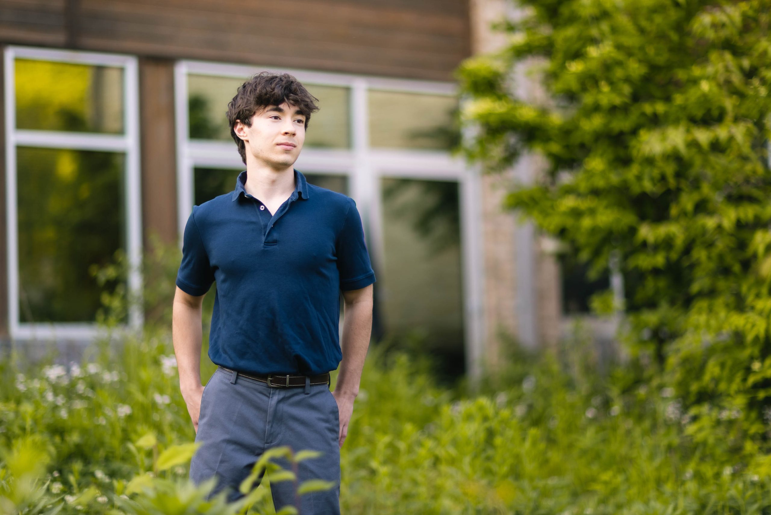 A young man in a blue shirt standing in front of a high school building.