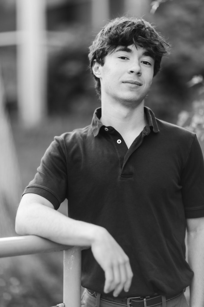 A black and white portrait of a young man leaning against a railing.