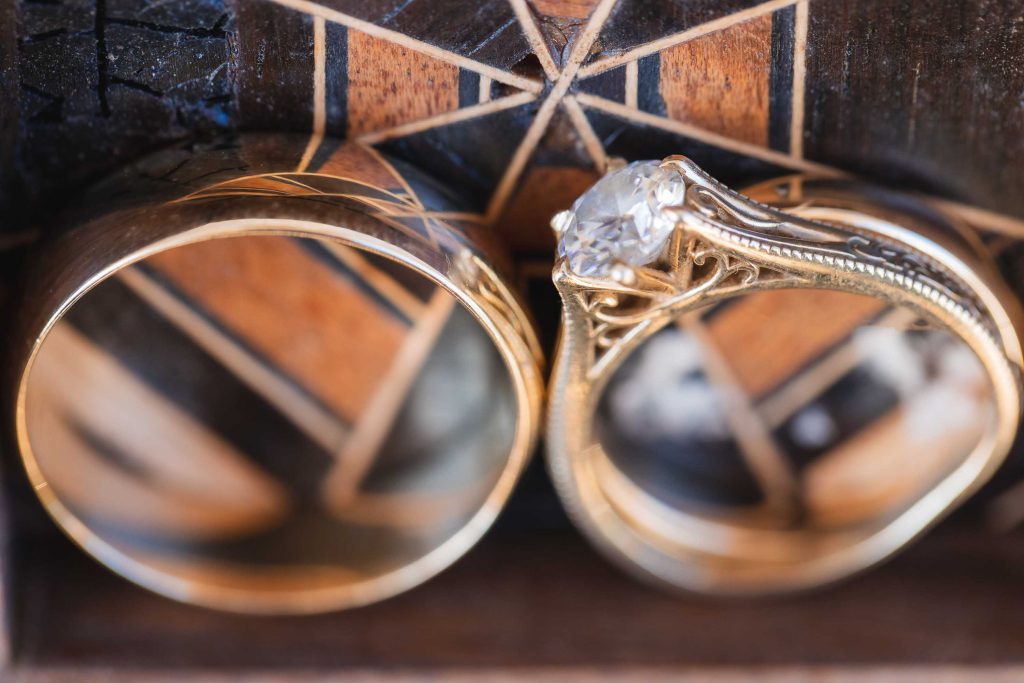 Detailed depiction of a wedding scene: two gold rings atop a wooden box.