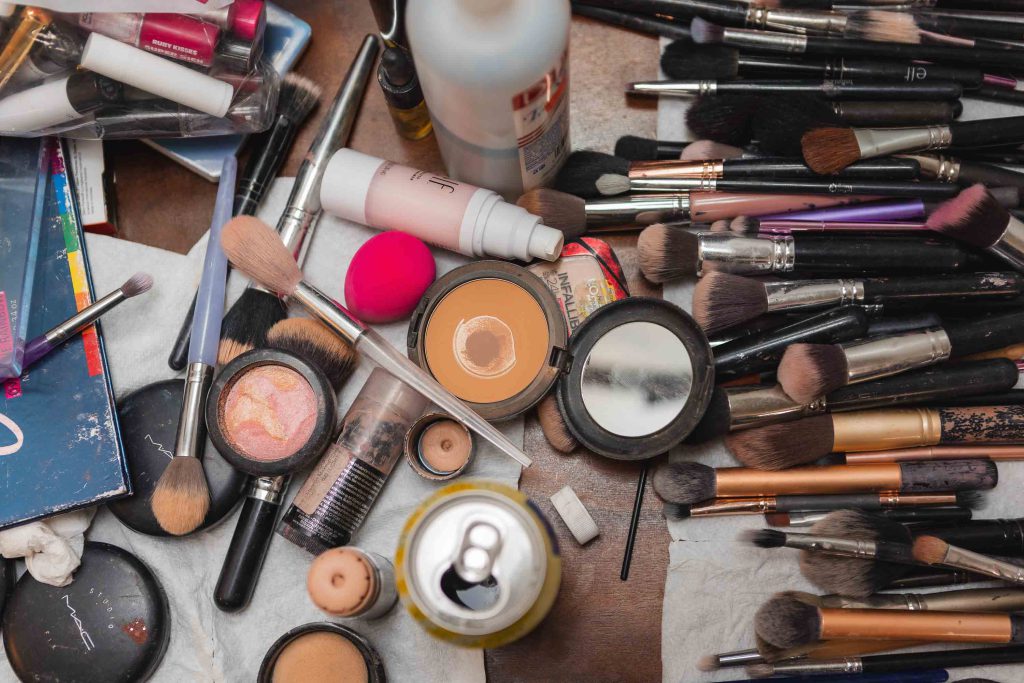 A pile of makeup brushes and cosmetics with wedding details on a table.