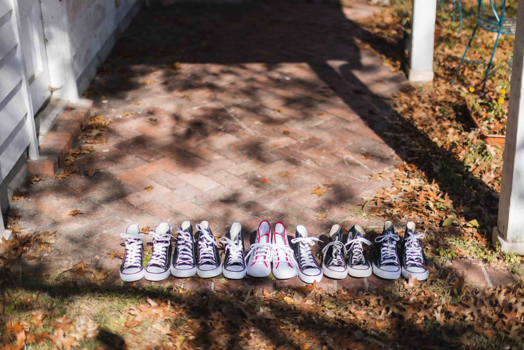 Five pairs of converse all star shoes lined up on a brick walkway with details for a wedding.