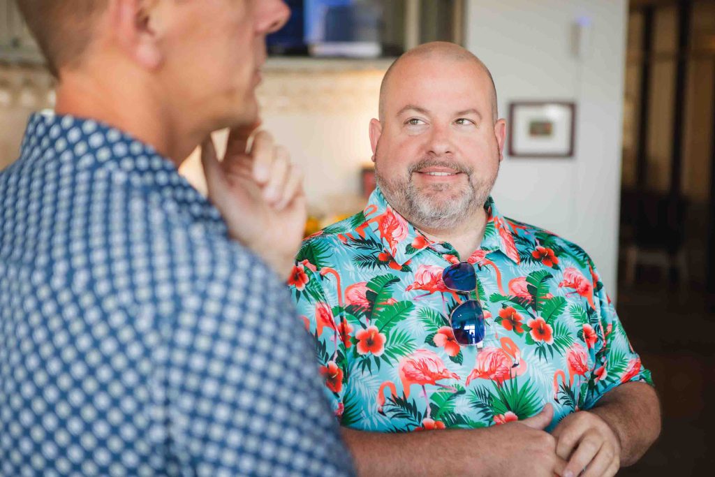 A man in a Hawaiian shirt chatting with another man at a birthday party.