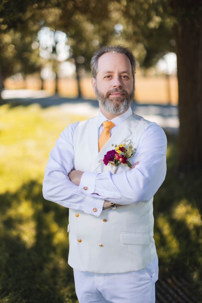 A man wearing a white tie stands in a field.